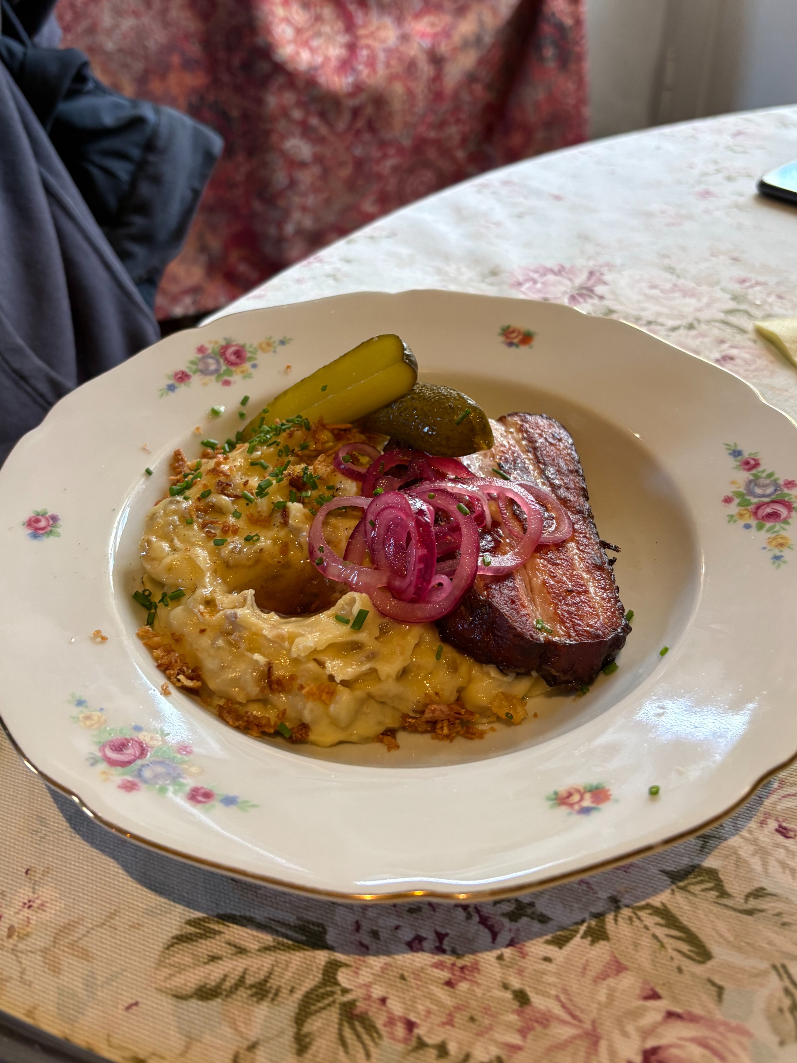 A plated meal with pickles and pickled onions on a floral tablecloth.