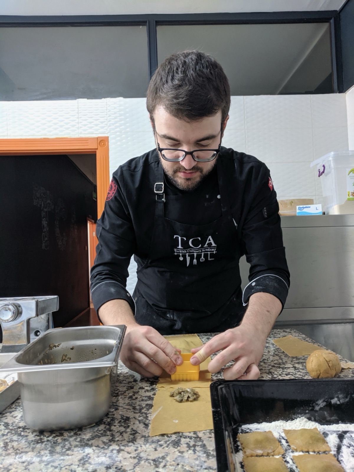 Emin focusing while shaping ravioli dough in a culinary school kitchen.