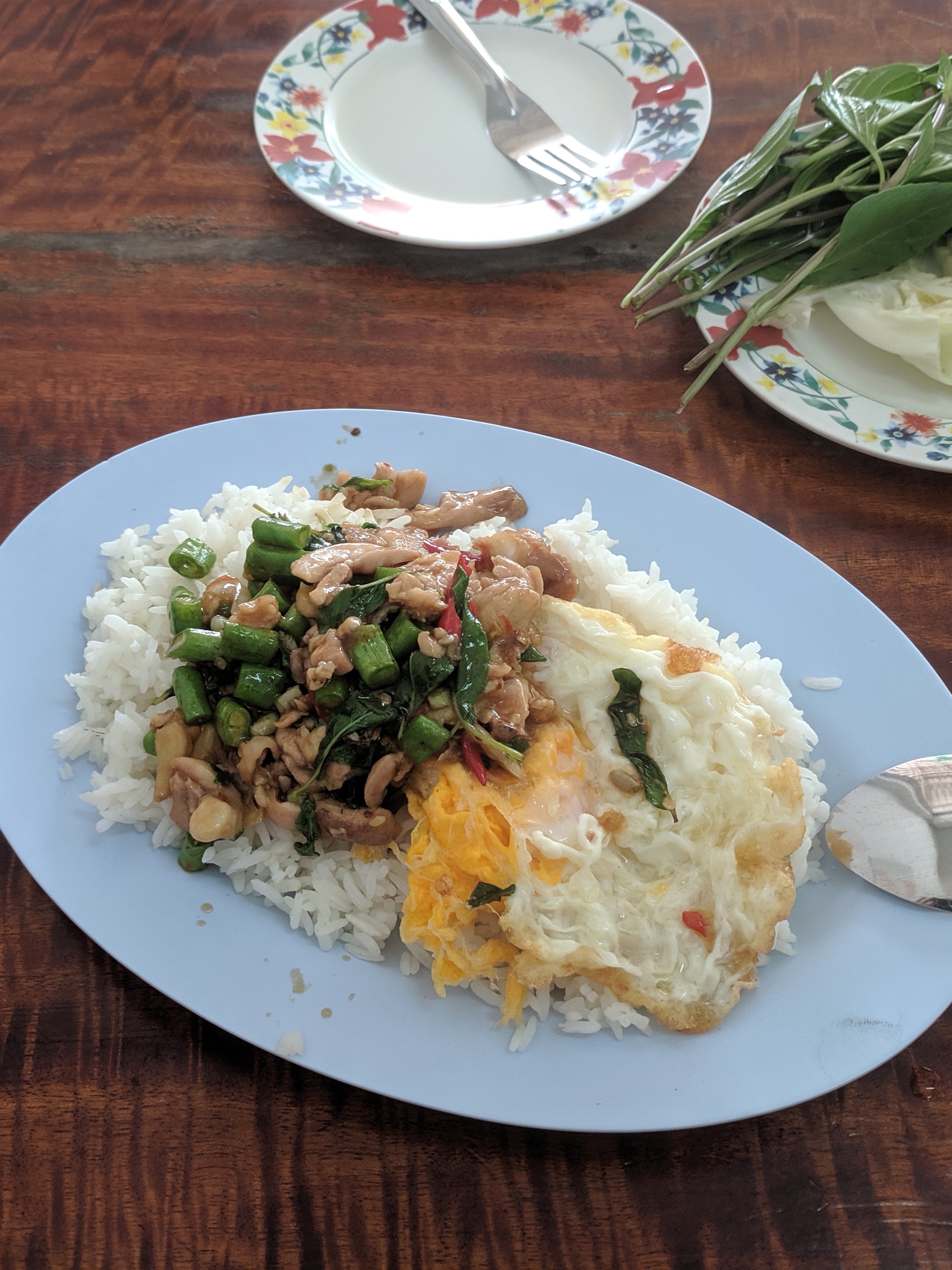 A plate of rice with basil chicken and fried egg on a wooden table.